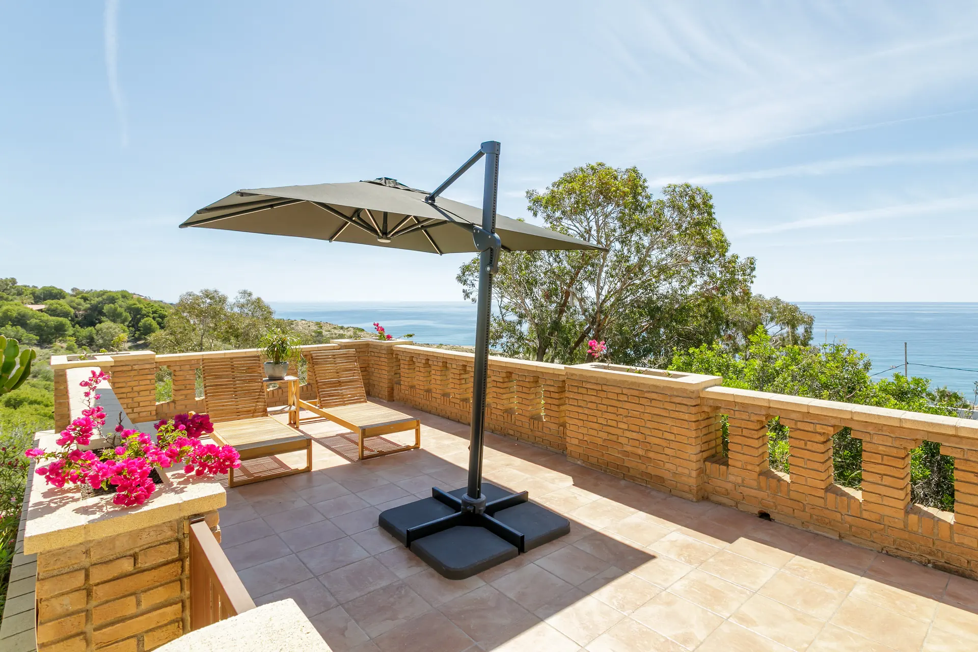 Zonneterras met parasol en ligbedden aan zee